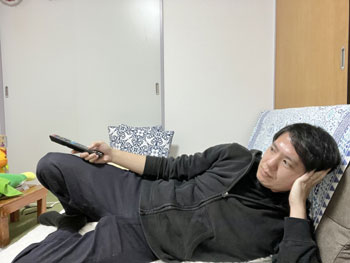 寝っ転がってテレビを見る男の画像